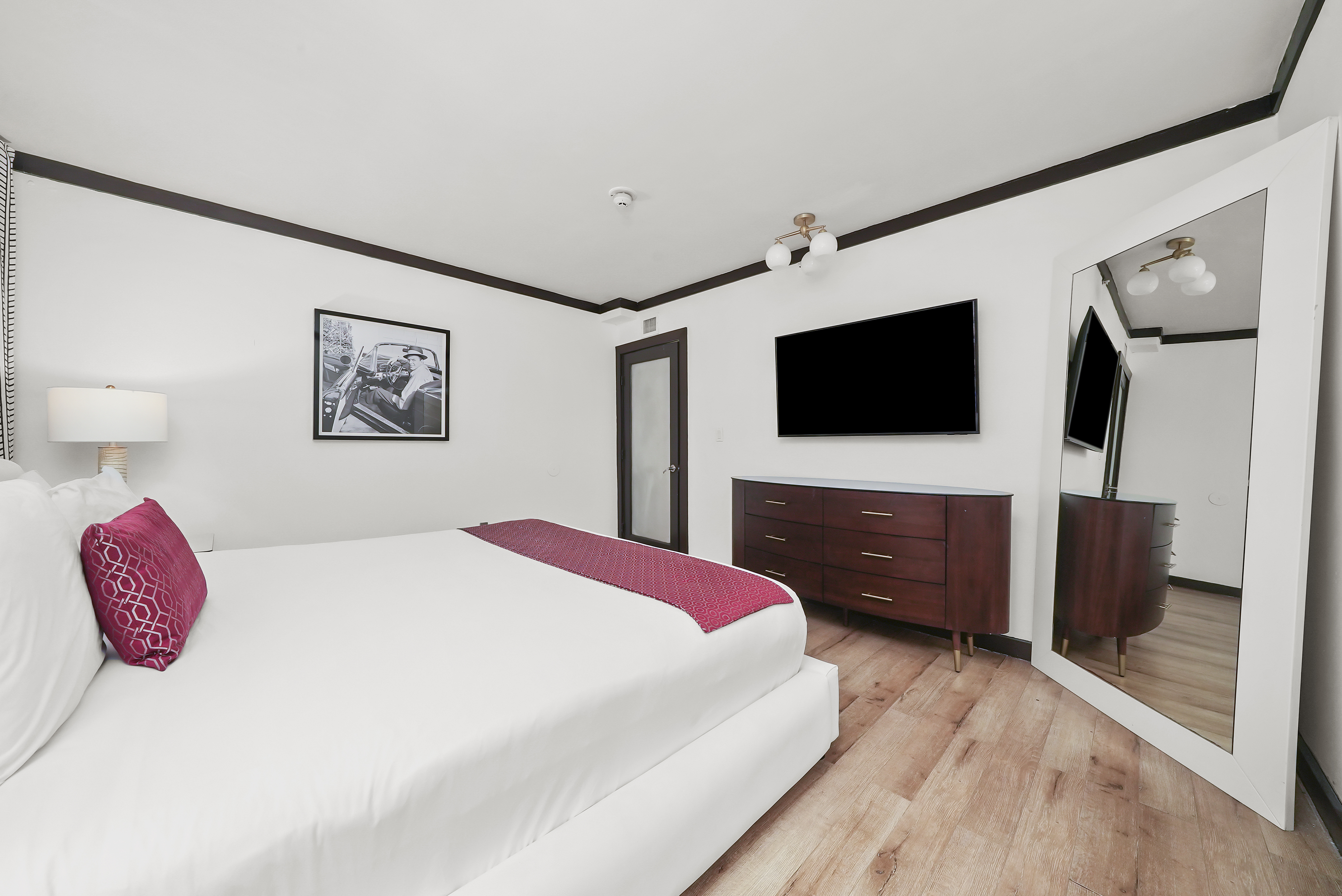 A wide view of a hotel room with a king-sized bed, dresser, mirror, and flat-screen TV.
