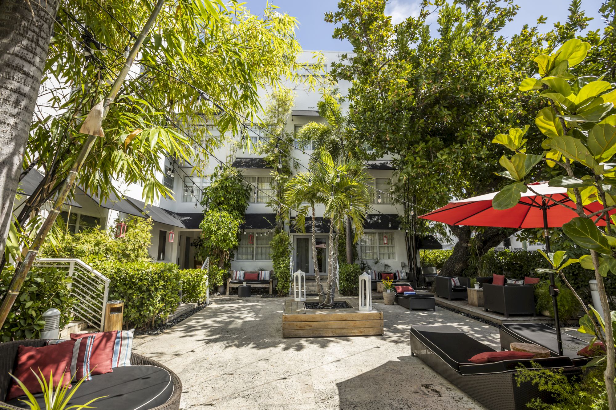 A sunny courtyard with lounge seating, greenery, and a red umbrella in a modern outdoor space.