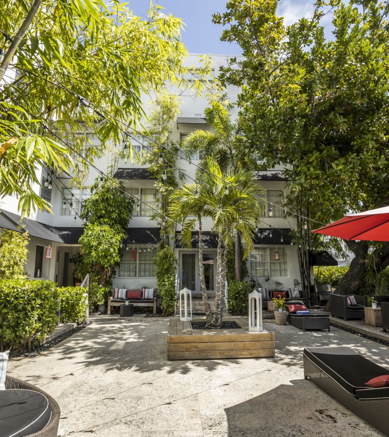 A white building with a courtyard featuring a palm tree, seating areas, and outdoor furniture.