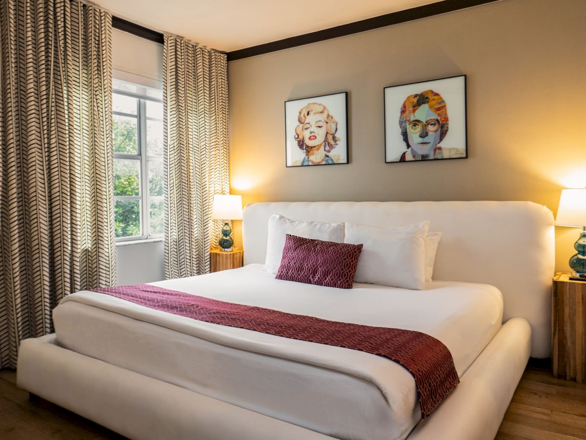 A modern bedroom with a white bed, patterned curtains, two framed portraits, and warm bedside lamps.