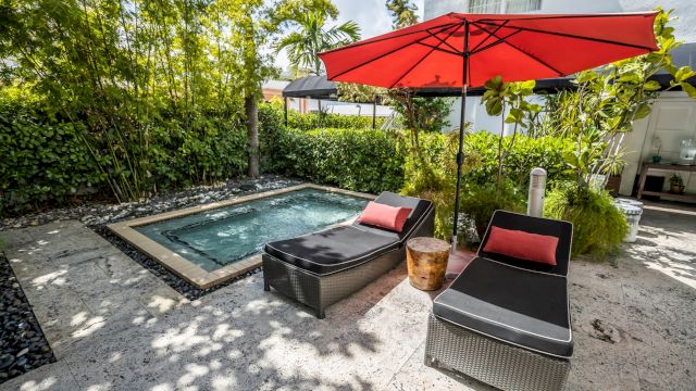 A small pool with two lounge chairs and a red umbrella