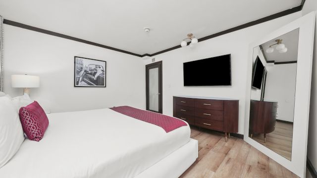 A wide view of a hotel room with a bed, TV, dresser, and mirror.